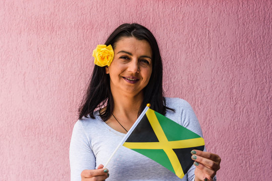 Woman holds flag of Jamaica in front of isolated wall background