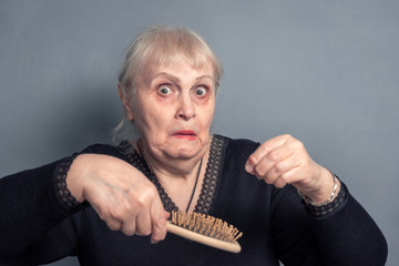 An elderly woman with a comb in her hand and a surprised look on a gray background. Barber...