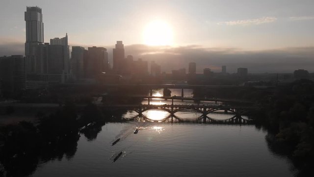 A drone slowly flies over the Colorado River and Lady Bird lake capturing a rowing crew working out  as the sun rises over the Austin, Texas skyline.