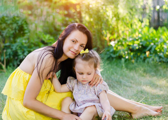Mom and daughter in the summer park. Mom in a yellow dress and daughter with a bow on her head toy hug and laugh in the sun