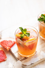Grapefruit cocktails with mint and ice. Cold summer citrus fresh beverage on light wooden background