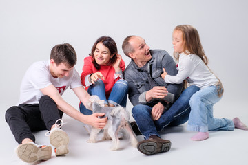 family plays with a dog on a light background on the floor