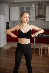 Fototapeta na wymiar Beautiful girl at home in black sportswear flexes her arms before training