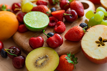 close up of mix of spring fruit on wooden table with natural light, strawberries, blueberries, lemon, lime, apple, kiwi, cherry, grape, all fresh and ripe, inviting and colorful,