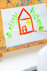 Hand of child drawing red house and words Stay Home with watercolors on the easel at home. Children's creativity concept.