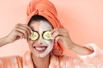 Young woman having skin care spa day at home - Happy girl applying cucumber facial cleanser mask -...