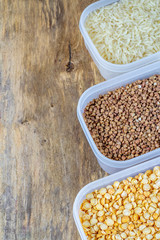 Raw rice, buckwheat and dry peas in plastic containers on wooden background