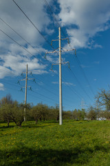 Fototapeta na wymiar High voltage power lines against a blue sky and white clouds. Summer sunny day, landscape in the city park.