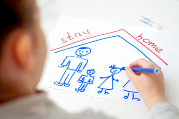 Child is drawing family with words Stay Home on white sheet of paper at home. Children's creativity in quarantine.