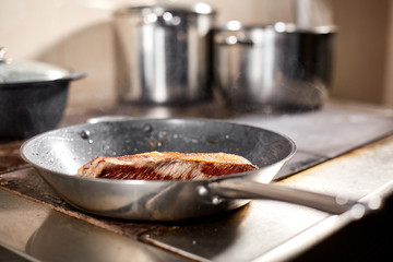 fried ribs of lamb. Cooking with fire in frying pan. Professional chef in a kitchen of restaurant cooking. Man frying food in flaming pan on hob.