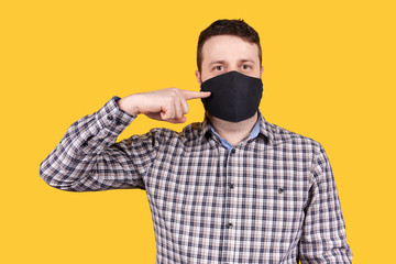 Obraz premium Man pointing on black face mask, isolated on orange background.