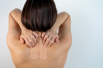 Kinesiology beige taping on the human back on a gray background with a copy space. Dynamic functional bandage taping on the girl's neck. Solution for back and neck pain. Headache.