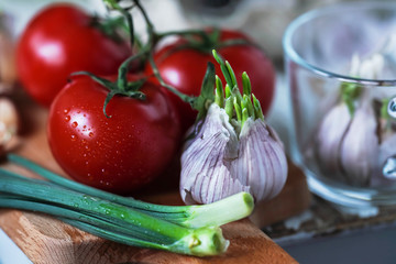tomatoes, and sprouted garlic and green onions on a wooden board close-up