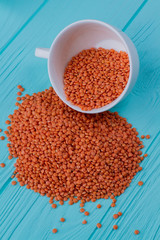 Spilled out pile of lentils groats. White cup on blue wood background.