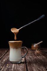 Iced Dalgona Coffee, a trendy fluffy creamy whipped coffee on a wooden table. Levitating the spoon with the foam. Close-up, vertical view.