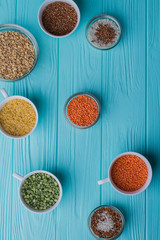 Many cups filled with various grains. Top view from above. Blue wood on background.