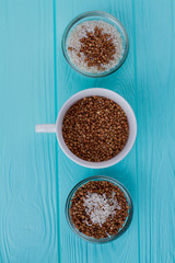 Three cups with buckwheat and rice on blue wood. View from above.