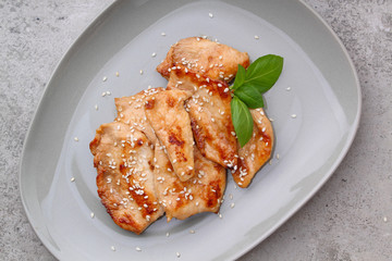 Fried chicken with soy sauce on a plate decorated with sesame seeds and basil, top view