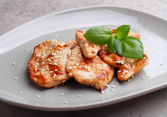Fried chicken with soy sauce on a plate decorated with sesame seeds and basil.