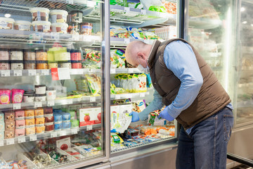 Moscow, Russia, 09/04/2020: A bald adult man in a medical mask and gloves chooses frozen foods in a supermarket. Precautions during the coronavirus pandemic pandemic.