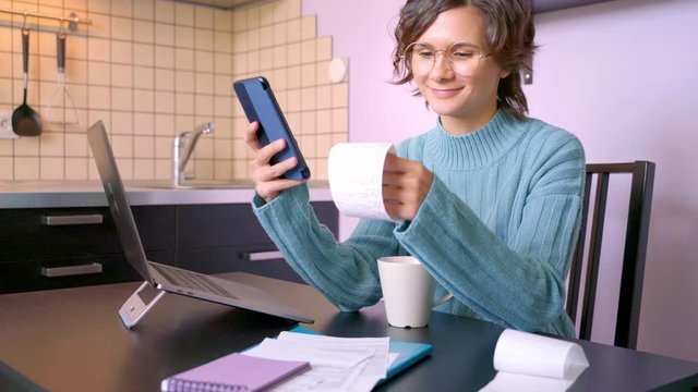 Video of young woman, looking at bills, thinking about how to pay all debts for rent school. Beautiful brunette girl with Bob hairstyle wears blue sweater. On table is laptop, coffee mug, Notepad home