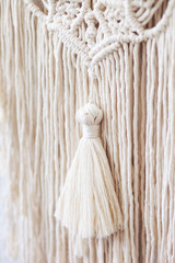 Handmade macrame  100% cotton wall decoration hanging on a white wall.  Macrame braiding and cotton threads. Details close up. Female hobby.