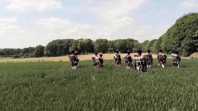 Aerial shot of French Napoleon soldiers walking in an open field surrounded by trees. Blue spring sky. Amazing drone shot.