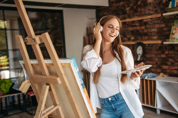 Beautiful girl singing and painting. Young beautiful woman painting artist while working in studio, listening to music in headphones