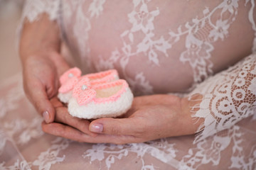 belly of a pregnant woman close-up and holding baby socks in her hand. the concept of love, care, and family