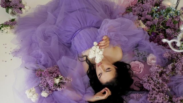 Beautiful woman lays on the floor in purple dress among white and pink flowers