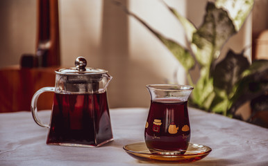 a glass teapot and tea glass filled with hibiscus herbal tea stay on the white table