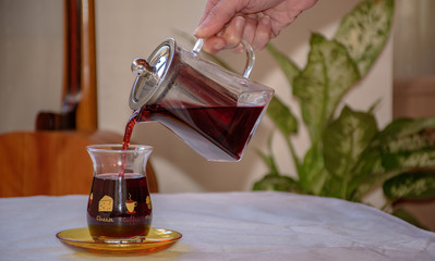 female hand pouring hibiscus tea into a classic turkish tea glass, closeup © mitre