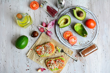 Cooking healthy and delicious food. Sandwiches with avocado and tomatoes, vegetables, olive oil, spices on a light wooden table. Top view
