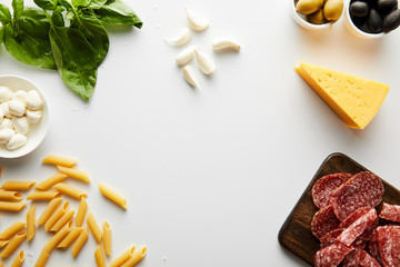 Top view of pasta, meat platter, cheese and ingredients on white background