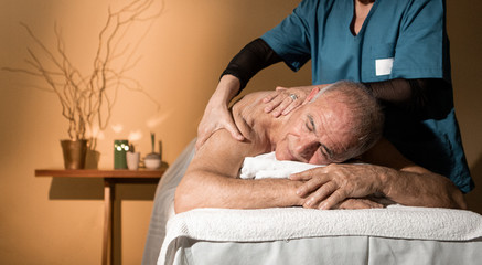 Uomo anziano in completo relax si fa massaggiare su un lettino da una massaggiatrice professionista...