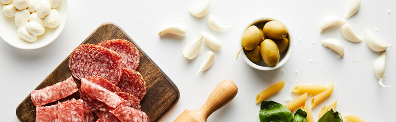 Panoramic orientation of meat platter, rolling pin, pasta, garlic and bowls with olives and mozzarella on white background