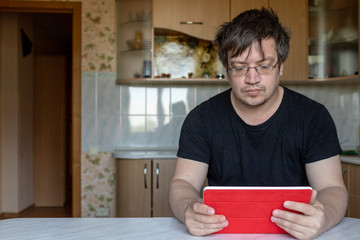 a man is sitting at a table at home. office at home. The  looking at the tablet. not a model, just an ordinary person. Man looking intently at the screen of the tablet