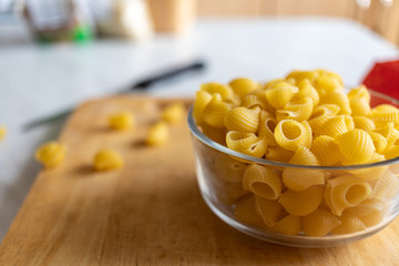 pasta in a clear deep bowl. it stands on a table and a wooden Board in the kitchen. near accidentally fallen fragments of paste. raw.