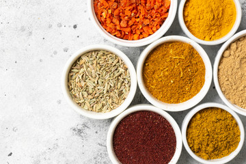 Spices and condiments in white bowls on a light gray table. Turmeric, ginger, curry, fennel and sumac in white bowls. Top view with space for text