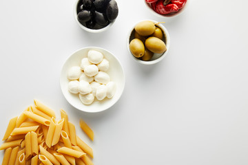 Top view of pasta and bowls with ingredients on white background