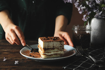 Girl takes a tiramisu with a shovel. Tasty cake on wooden background