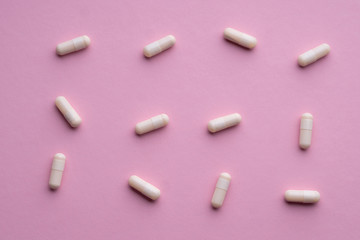 A lot of white pills on a pink background.