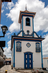 Front view to small beautiful chapel in white and blue against blue sky with white clouds in...