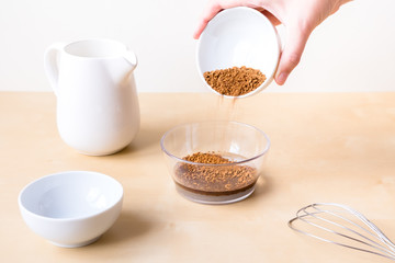 How to make dalgon coffee. Step by step photo instruction. Step 3. Add coffee and sugar to the water. Ingredients - instant coffee, sugar, water, milk and a whisk for whipping on a wooden background