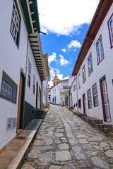 Narrow cobblestone lane with traditional houses and blue sky and white clouds in Diamantina, Minas Gerais, Brazil
