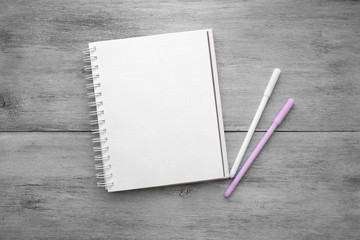 White notebook, two pens on a white wooden table top view of flat objects