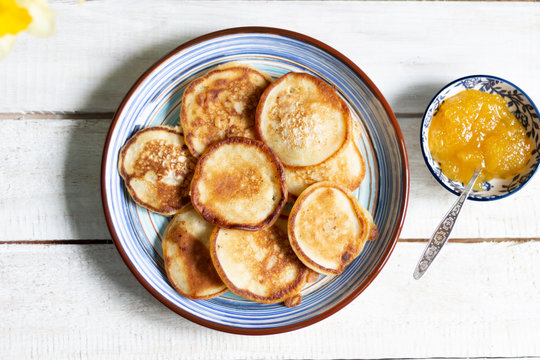 Fritters in blue plate, honey with spoon, daffodile on white wooden background