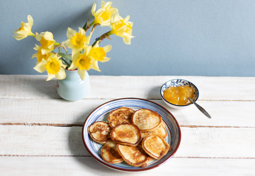 Fritters in blue plate, honey with spoon, daffodile flowers bouquet on white wooden background