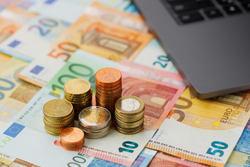 Columns euro coins in focus close-up on a background of euro banknotes and a laptop. The background is blurry.