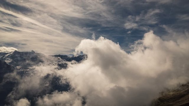 Time lapse of clouds moving over a snowy alpine mountain landscape overlooking a valley below. Captured in the mountains of Grindelwald in Switzerland.